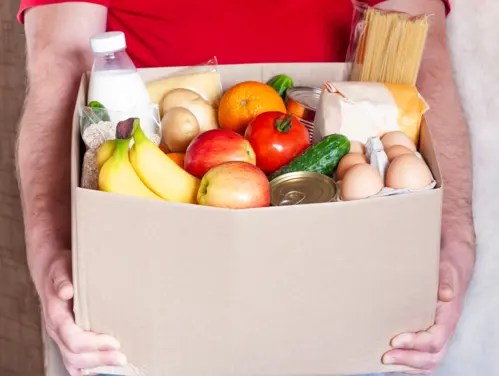 Box of food including bananas, milk, vegetables, and eggs.