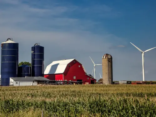 Landscape of Iowa farm with red barn, blue silos and windmills.